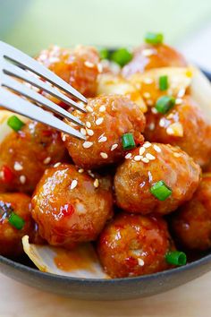 a plate full of meatballs covered in sauce and green onions with a fork sticking out of it