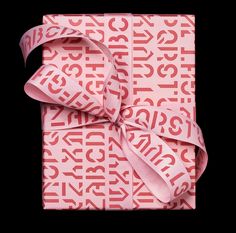 a pink wrapped gift box with white lettering on it and a ribbon tied around the top