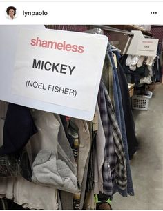 a sign that says shame mickey noel fisher in front of clothes hanging on racks at a clothing store