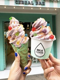 two people holding up ice cream cones in front of a building