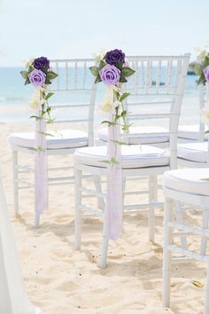 white chairs with purple flowers on them are set up in the sand at the beach