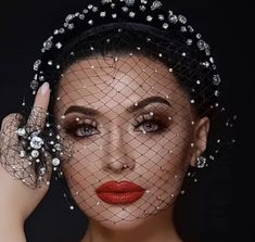 a woman wearing a veil and holding her hand up to her face with pearls on it