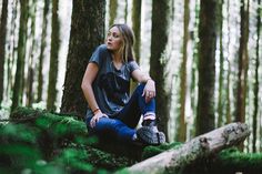 a woman sitting on top of a log in the middle of a forest filled with trees