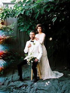 a bride and groom sitting on a chair in front of a tree with sunbeams