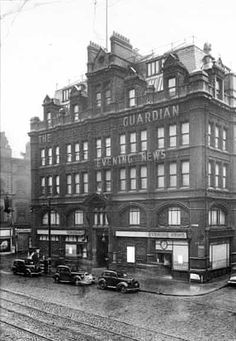 an old black and white photo of cars parked in front of a building on the street