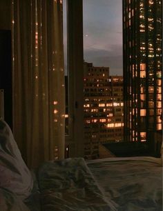 a bed sitting in front of a window next to a night time cityscape