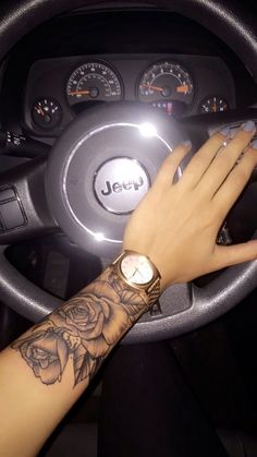 a woman's hand on the steering wheel of a car with a wrist tattoo