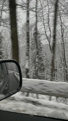 the rear view mirror of a car on a snowy road with trees in the background