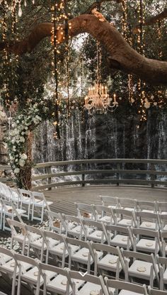 an outdoor ceremony setup with white chairs and chandelier hanging from the tree branches