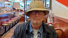 a man wearing a hat and glasses sitting at a table in front of a restaurant