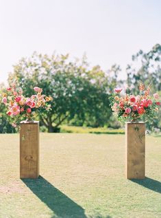 two wooden vases filled with flowers sitting on top of a grass covered field next to trees