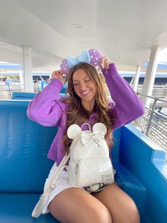 a woman sitting on a blue bench with a white backpack and purple shirt over her head