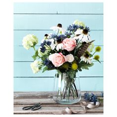 a vase filled with lots of flowers on top of a wooden table next to scissors