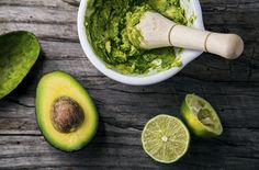 an avocado is in a white bowl next to sliced limes and a wooden spoon