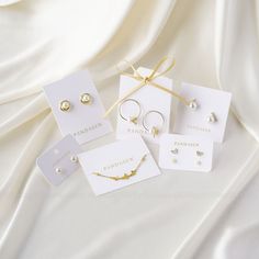 four pairs of earrings are on display in front of a white background with gold ribbon