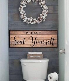 a toilet in a bathroom with a wooden sign above it that says please seat yourself