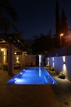 an outdoor swimming pool at night with lights on the wall and plants in pots next to it