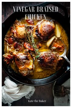 a skillet filled with chicken and vegetables on top of a wooden table next to bread