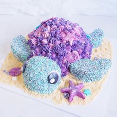 there is a cake made to look like a turtle on the beach with purple and blue frosting