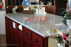 a kitchen island with marble counter tops and red cabinets in the background, surrounded by vases filled with flowers