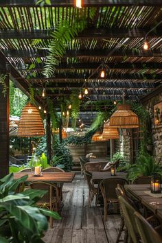 an outdoor dining area with wooden tables and wicker lamps hanging from the ceiling, surrounded by greenery