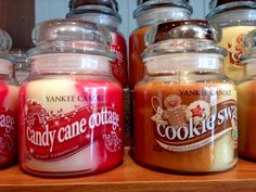 candles are lined up on a shelf in front of glass jars filled with candy canes