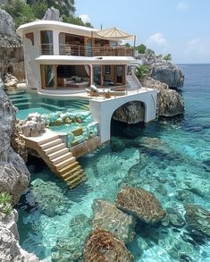 a house that is sitting in the water next to some rocks and clear blue water