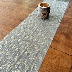 a table runner with a cup on it sitting on top of a wooden floor next to a window