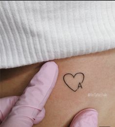 a person holding their stomach with a heart tattoo on the side of her stomach,