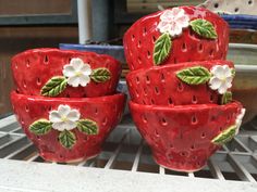 four ceramic strawberries with flowers on them sitting on a shelf next to a bowl