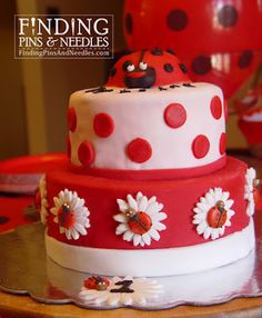 a red and white cake with ladybug decorations on the top is sitting on a table