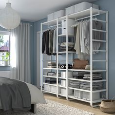 a bedroom with blue walls and white shelving unit in the corner, filled with clothes