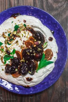 a blue plate topped with whipped cream covered in figs and nuts on top of a wooden table