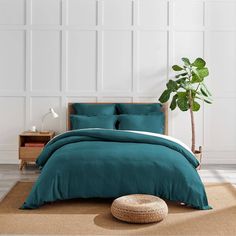 a bed with teal colored linens and pillows in a white room next to a potted plant