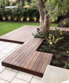 a wooden bench sitting on top of a lush green field next to a tree and shrubbery