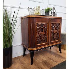 a wooden cabinet sitting on top of a hard wood floor next to a potted plant