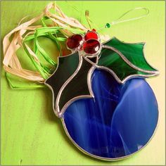 a stained glass ornament with a holly decoration on it's side, sitting on a green surface