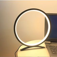 a laptop computer sitting on top of a desk next to a light up ring lamp