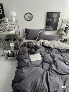 an unmade bed in a bedroom with a clock on the wall