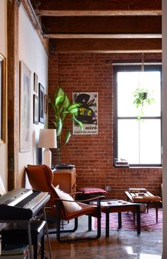 a living room filled with furniture and a piano in front of a large brick wall