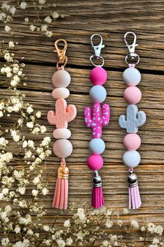 three keychains with different designs and colors are hanging on a wooden table next to flowers