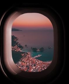 an airplane window looking out at the water and land below it, with buildings on either side