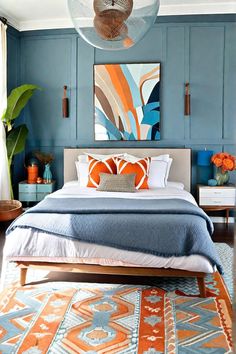 a bedroom with blue walls, orange and white decor and an art work on the wall