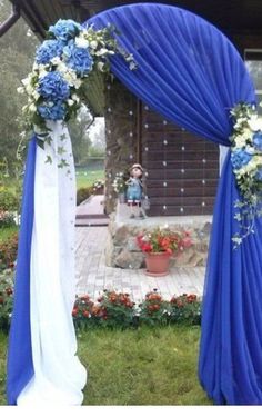 a blue and white wedding arch with flowers on the top, in front of a house