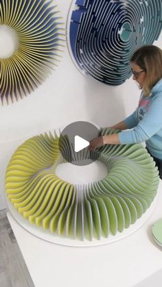 a woman is working on an art piece in the middle of a room with two circular sculptures behind her