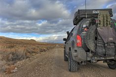 the back end of a vehicle on a dirt road with clouds in the sky above