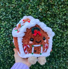 a hand holding up a small gingerbread ornament in front of a hedge