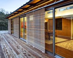 a wooden deck with sliding glass doors leading to a dining room and patio area that is lit up at night