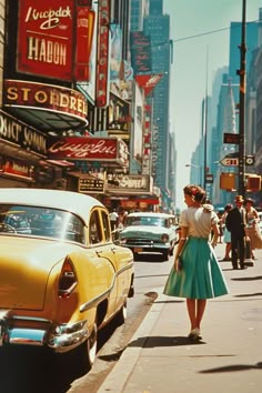 a woman in a green dress is standing on the sidewalk next to an old yellow car