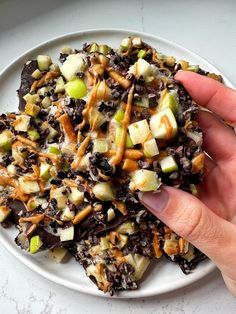 a hand is picking up an apple salad on a white plate with caramel drizzle